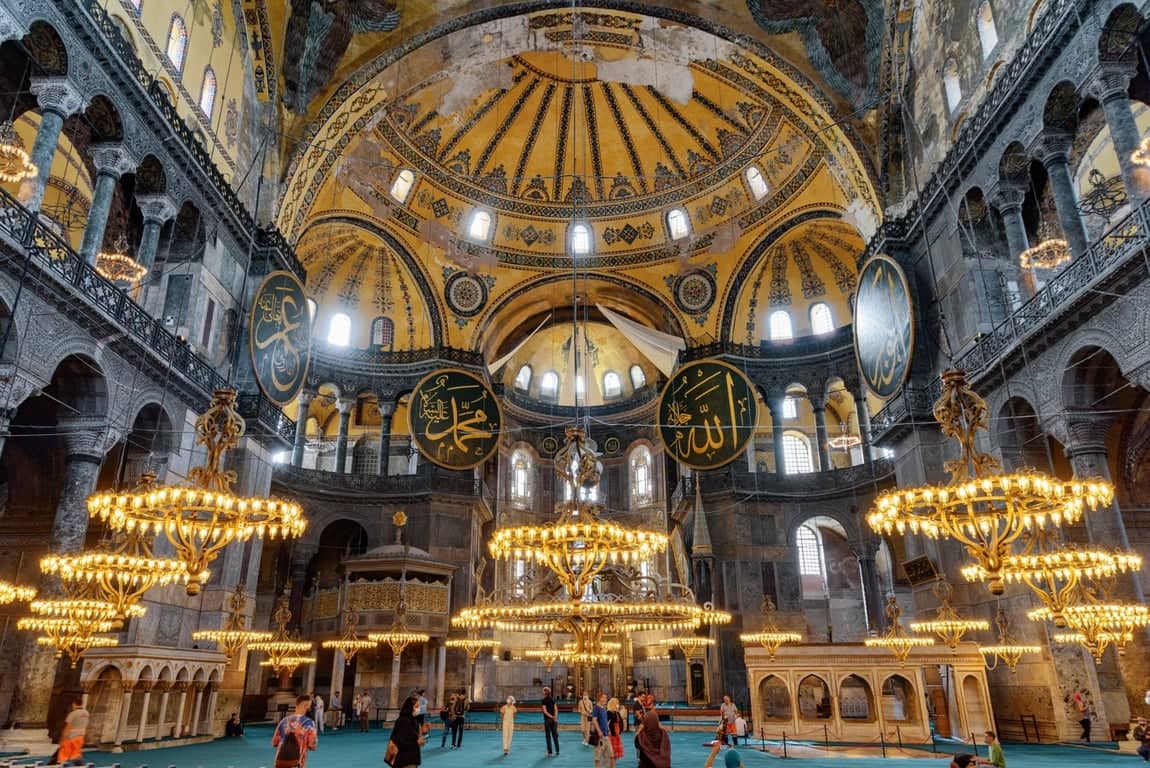 Chandeliers and marble interior of Hagia Sophia, visitors looking up during entry