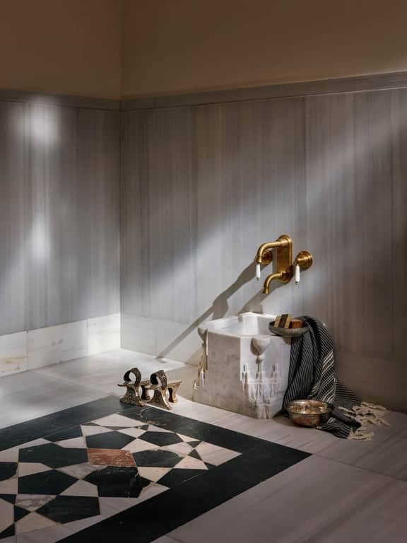 Close-up of brass taps and bowls beside geometric marble floor design